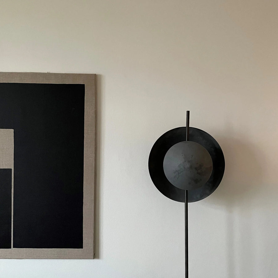 Modern floor lamp with black circular design on a white wall next to framed artwork.