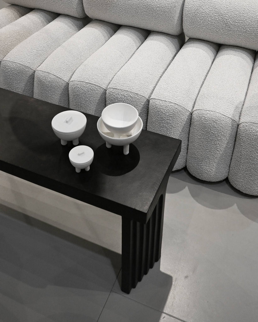 Black coffee table with white ceramic bowls and duck jars in front of a gray textured sofa from 101 Copenhagen at Spacio retail stores in Mumbai & Kolkata. 