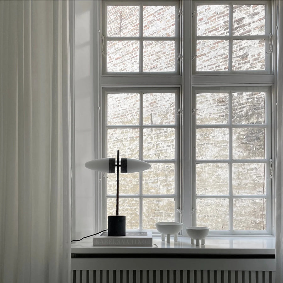 Modern interior with a lamp and decorative bowls on a windowsill with a brick wall view.