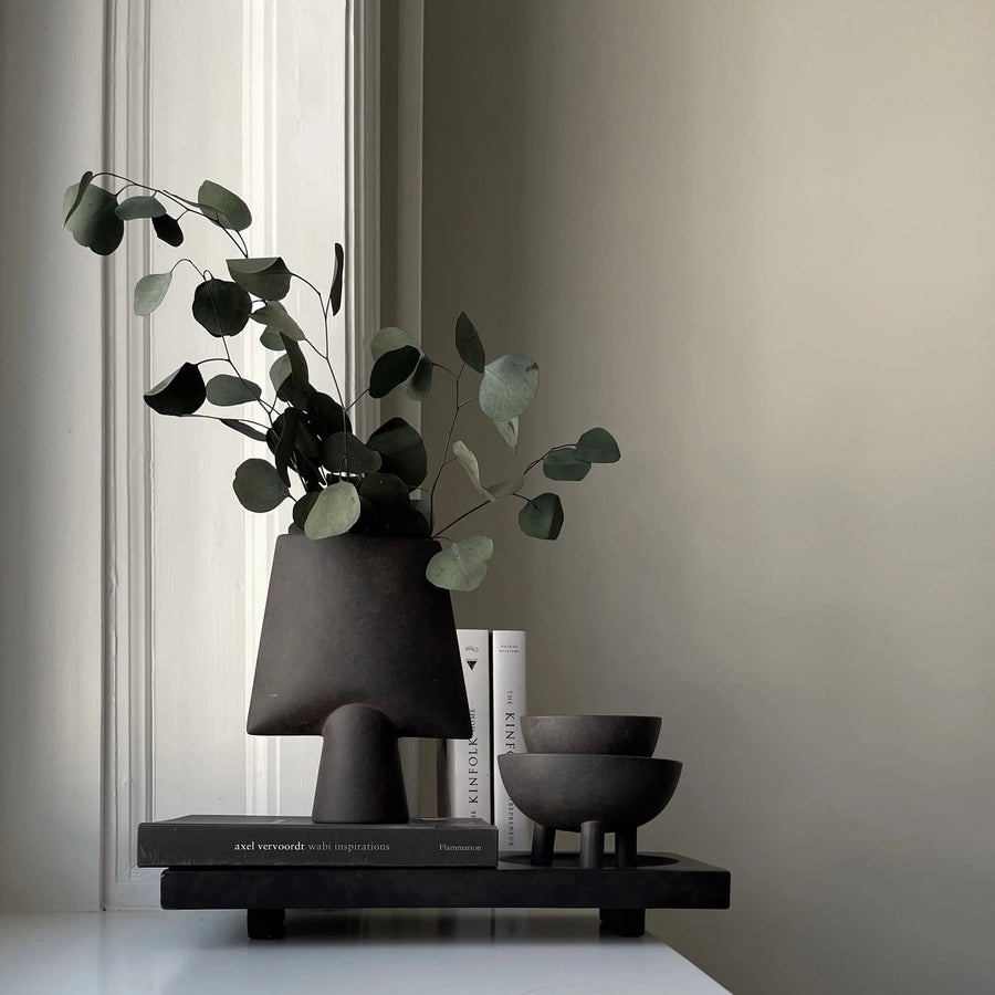 Decorative setup with a black vase, books, and bowls on a shelf against a neutral wall from 101 Copenhagen at Spacio retail stores in Mumbai & Kolkata. 