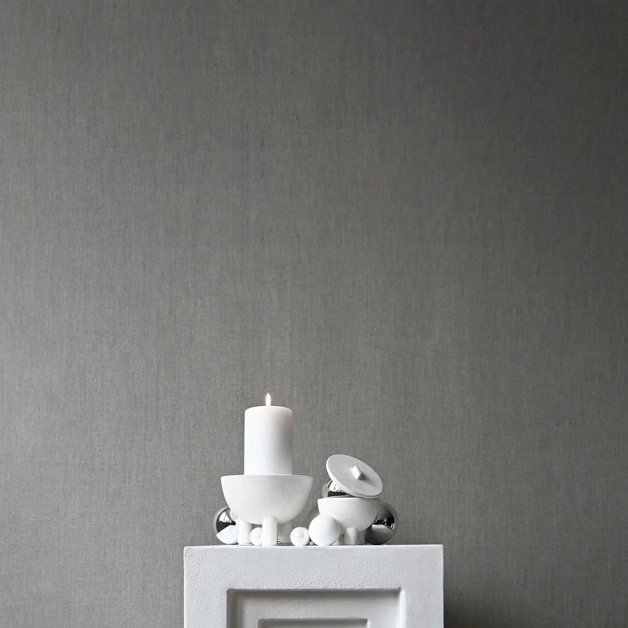 White candle and decorative items on a gray pedestal against a gray wall from 101 Copenhagen at Spacio retail stores in Mumbai & Kolkata. 