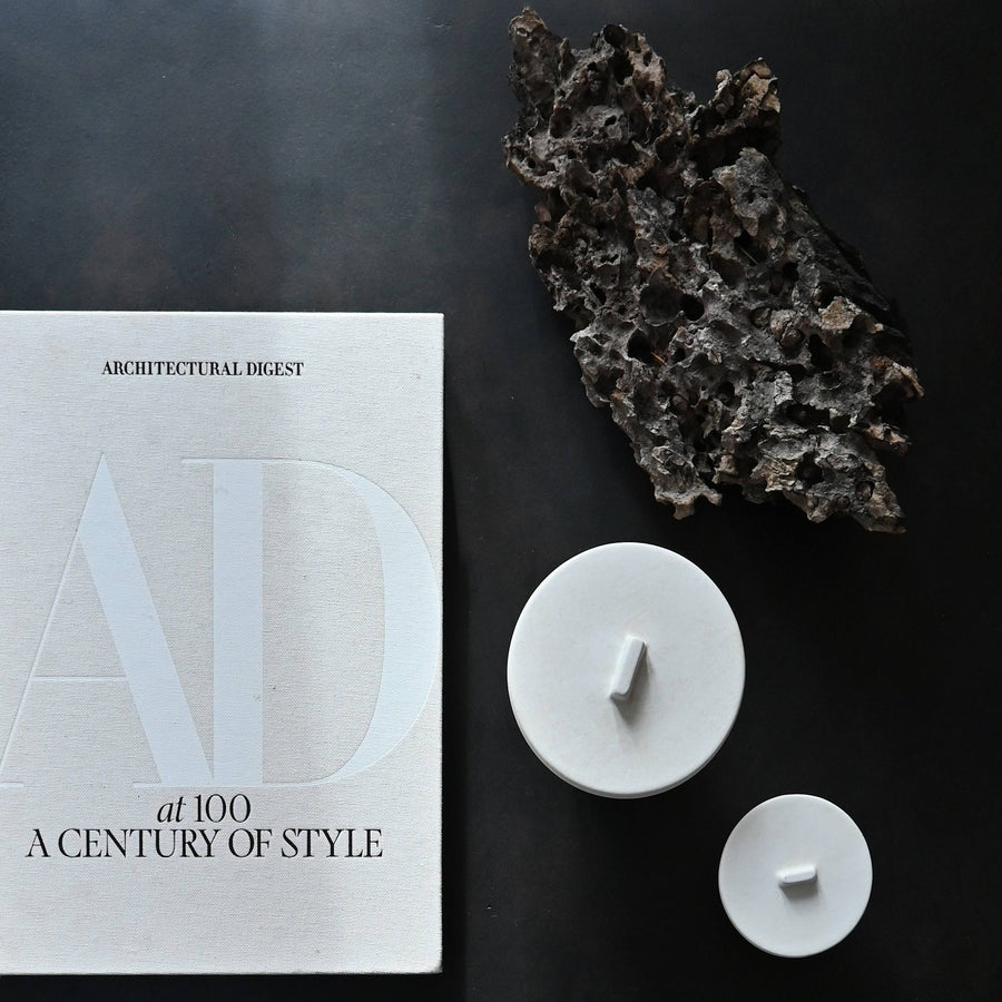 White ceramic jars with lids on a dark surface with 'Architectural Digest' magazine  from 101 Copenhagen at Spacio retail stores in Mumbai & Kolkata. 