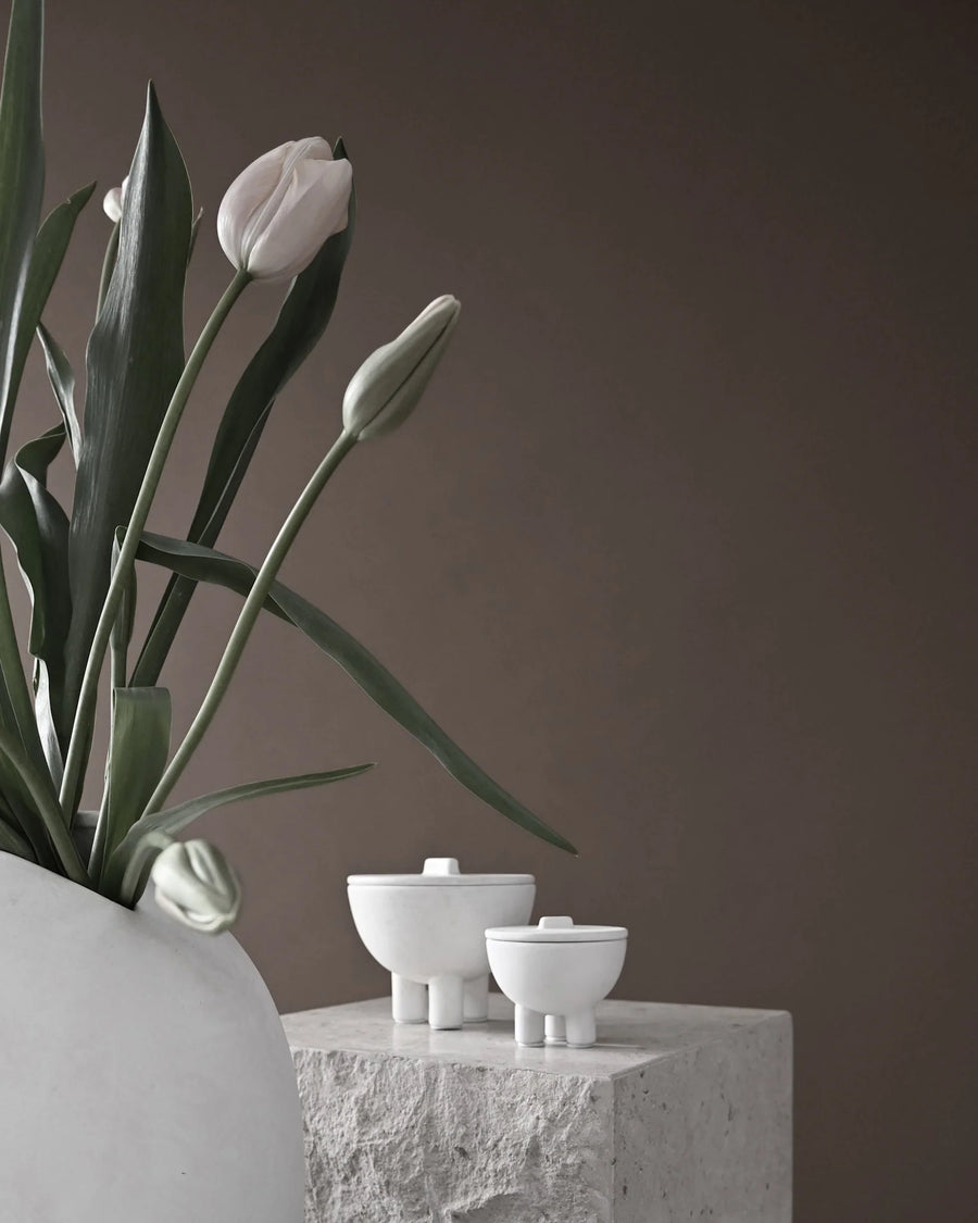 White tulips in a vase with three small white bowls on a stone surface against a brown background from 101 Copenhagen at Spacio retail stores in Mumbai & Kolkata. 