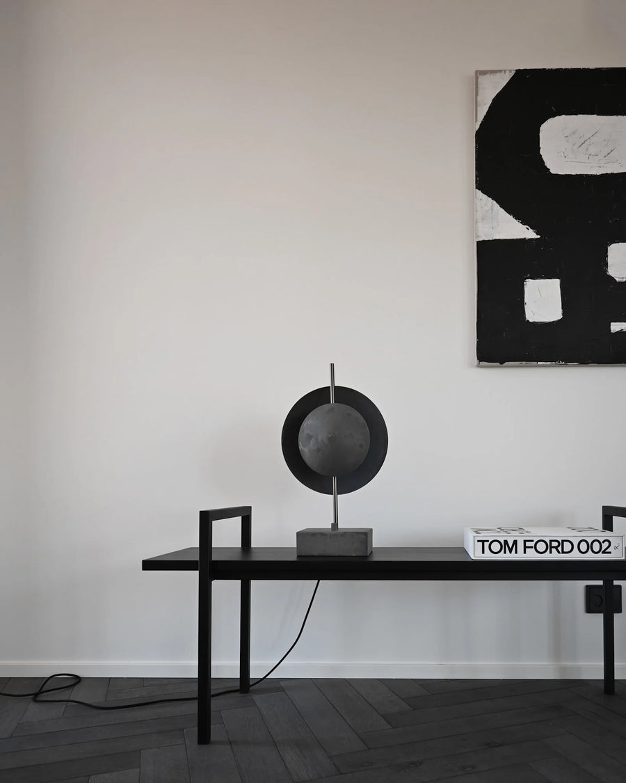 Modern interior with a black table and lamp against a white wall with abstract art.