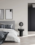 Modern bedroom with gray bed, black nightstand, and abstract art on the wall.