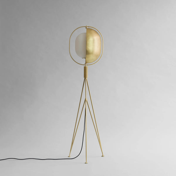 Brass floor lamp with a white shade on a gray background