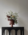Vase with flowers on a black chair against a plain wall