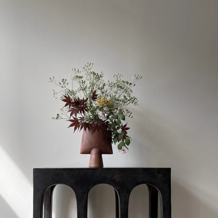 Vase with flowers on a black chair against a plain wall