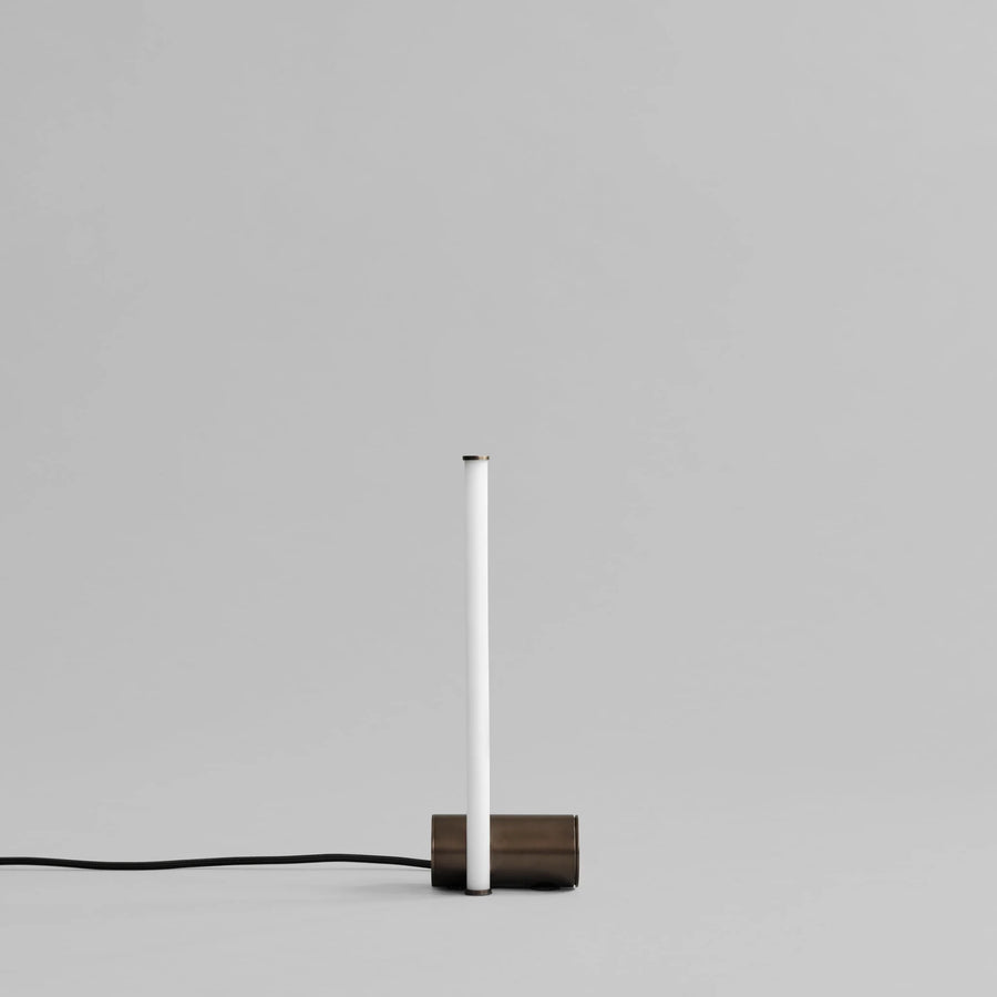 Minimalist table lamp with a white cylindrical shade and wooden base on a gray background
