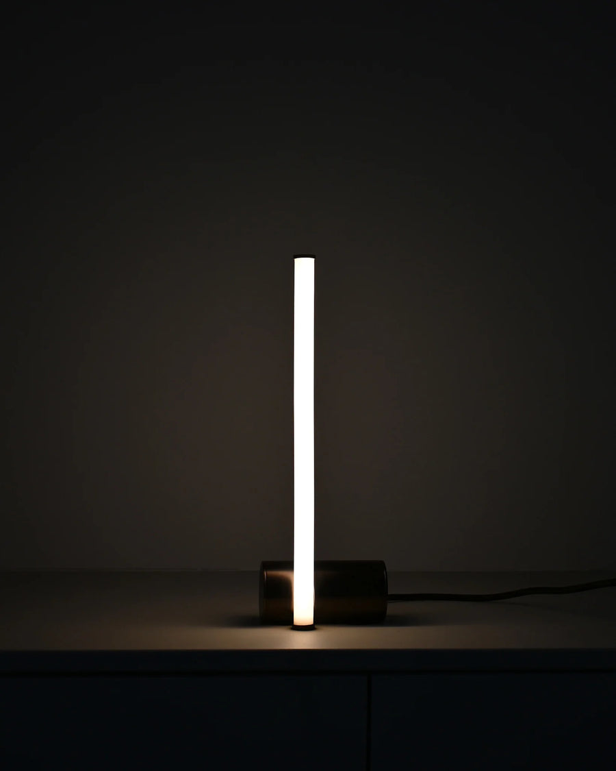 Modern table lamp with a long, thin light source on a dark background