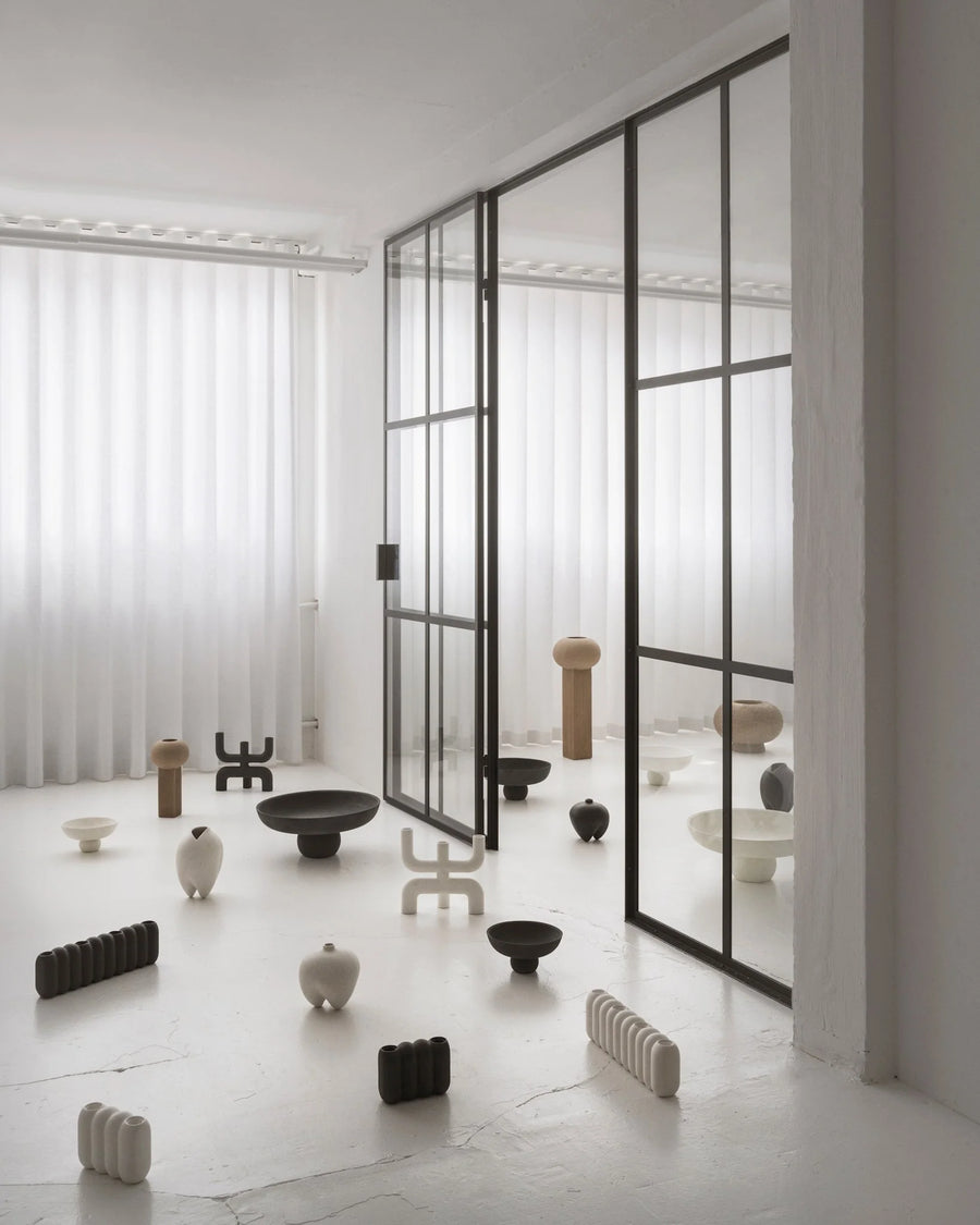 Modern interior with glass walls and various ceramic sculptures on a light floor.