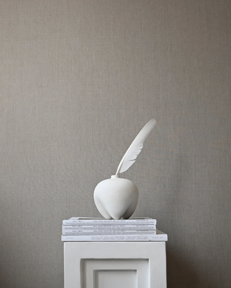 White sculpture of an apple with a feather on a gray pedestal against a gray wall from 101 Copenhagen at Spacio retail stores in Mumbai & Kolkata. 