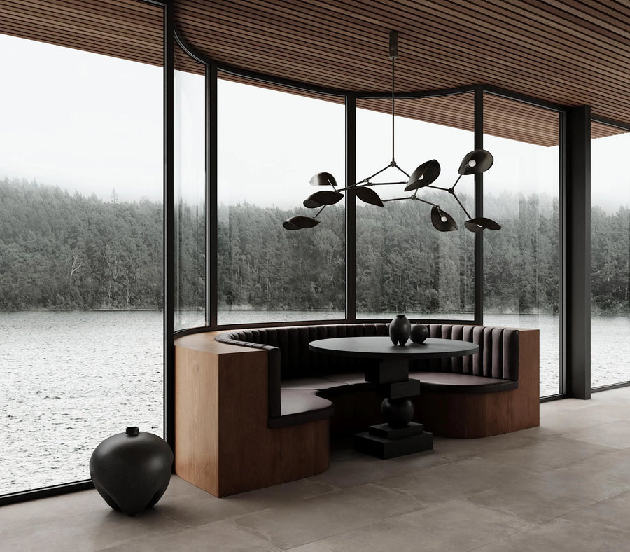 Modern interior with a round dining table and bench seating by large windows with a view of water and trees.