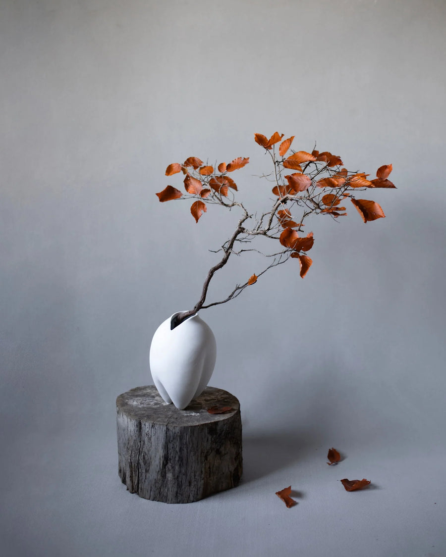 White vase with a branch and orange leaves on a gray background from 101 Copenhagen at Spacio retail stores in Mumbai & Kolkata. 
