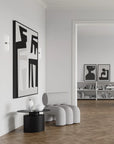 Modern interior with a gray armchair, black side table, and abstract wall art.