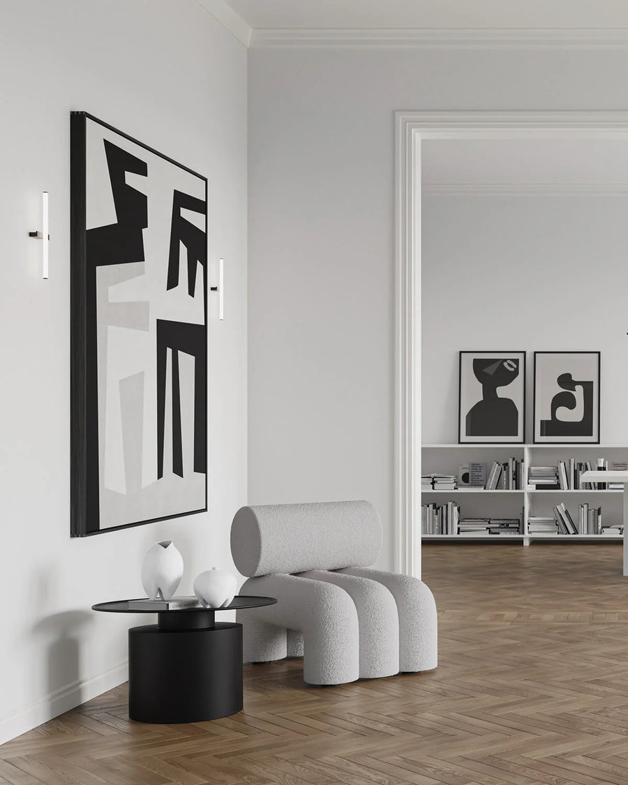 Modern interior with a gray armchair, black side table, and abstract wall art.