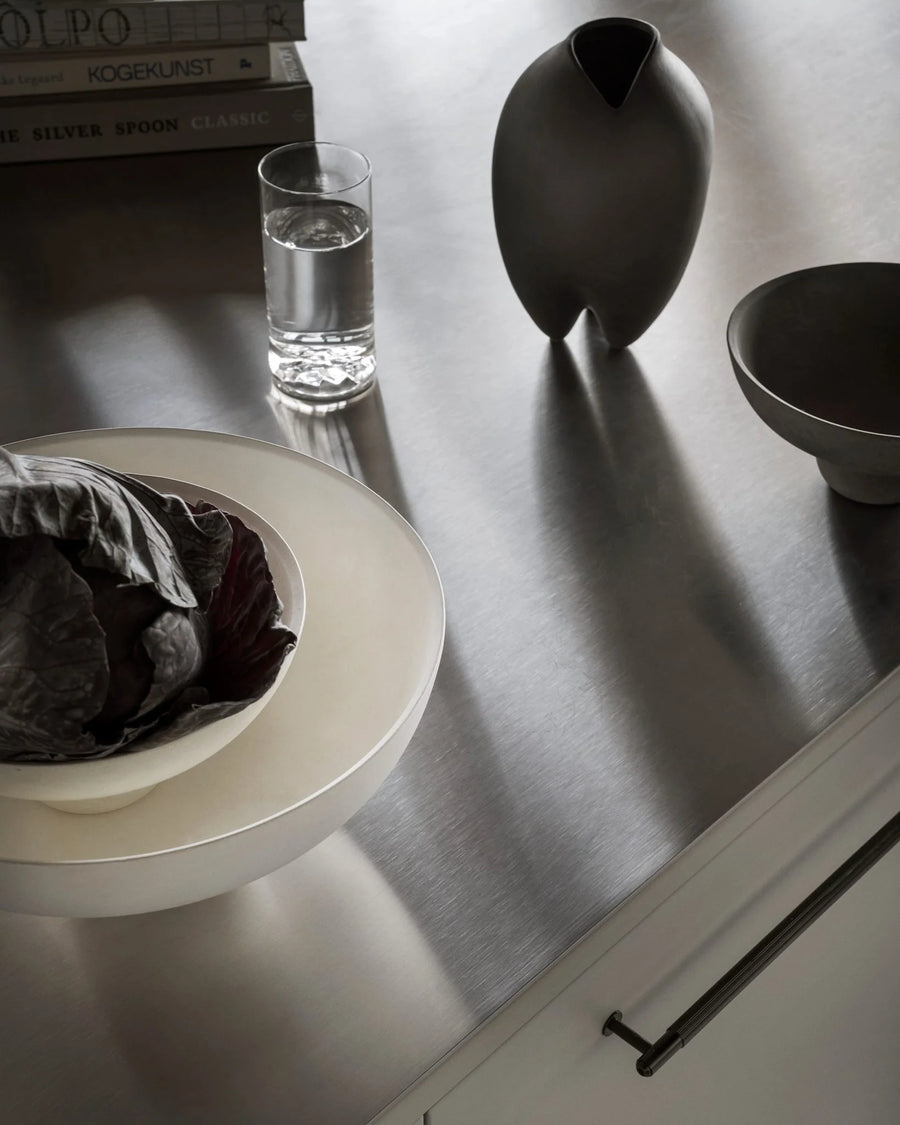 Table setting with a bowl, glass of water, and vase on a reflective surface.