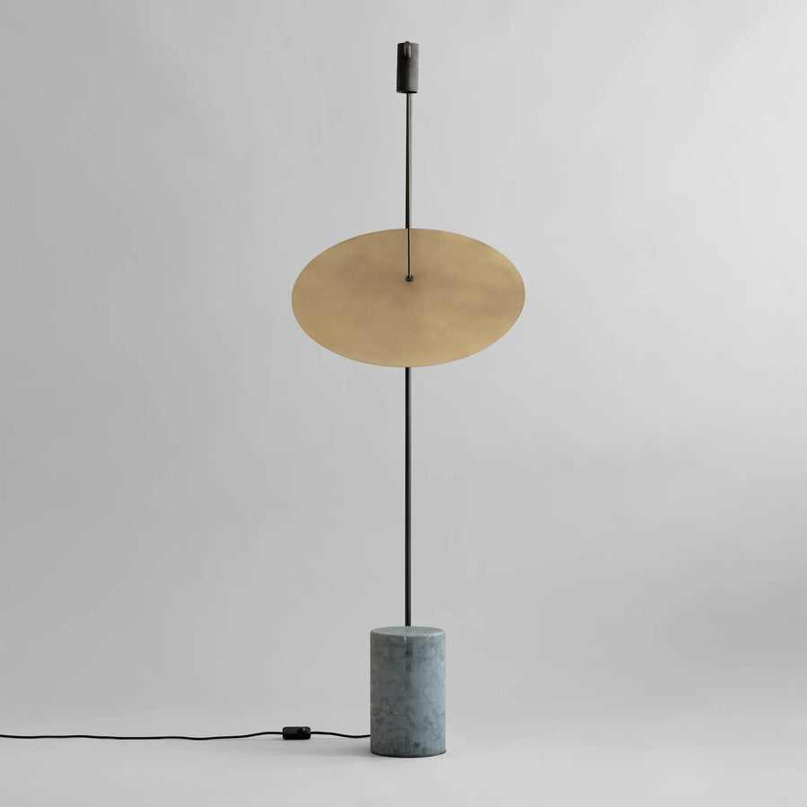 Modern floor lamp with brass disc shade and concrete base on a gray background