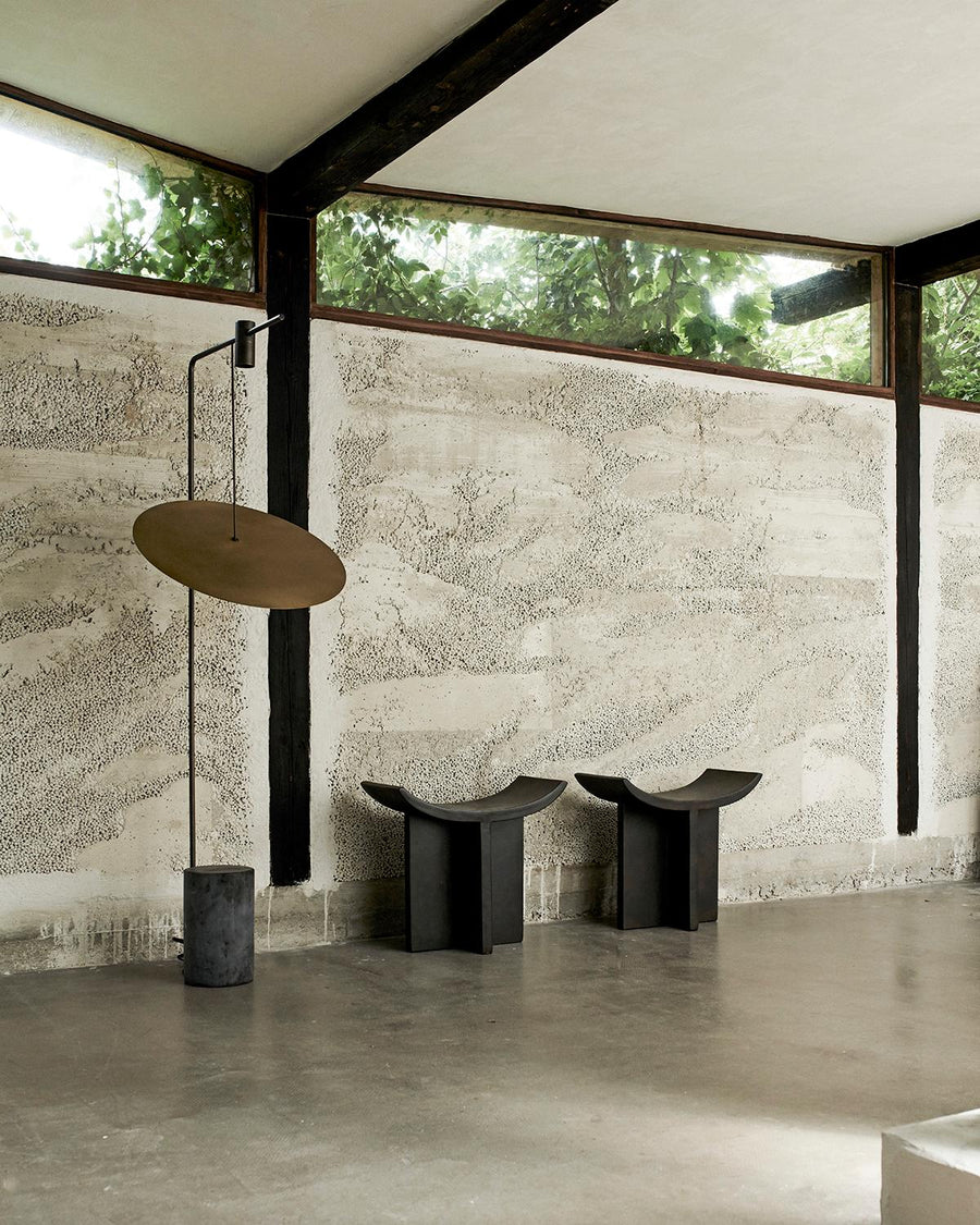 Modern interior with a floor lamp and two stools against a textured wall.