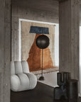 Modern interior with a gray armchair, black floor lamp, and abstract wall art.