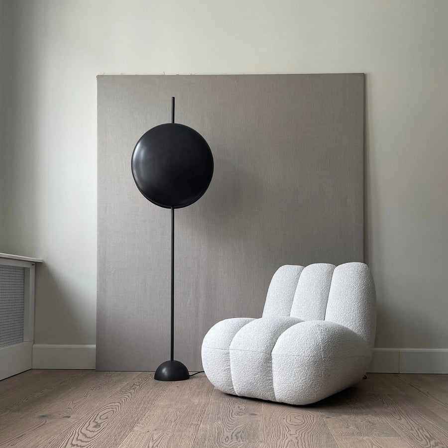 Modern black floor lamp next to a white textured armchair in a minimalistic room.
