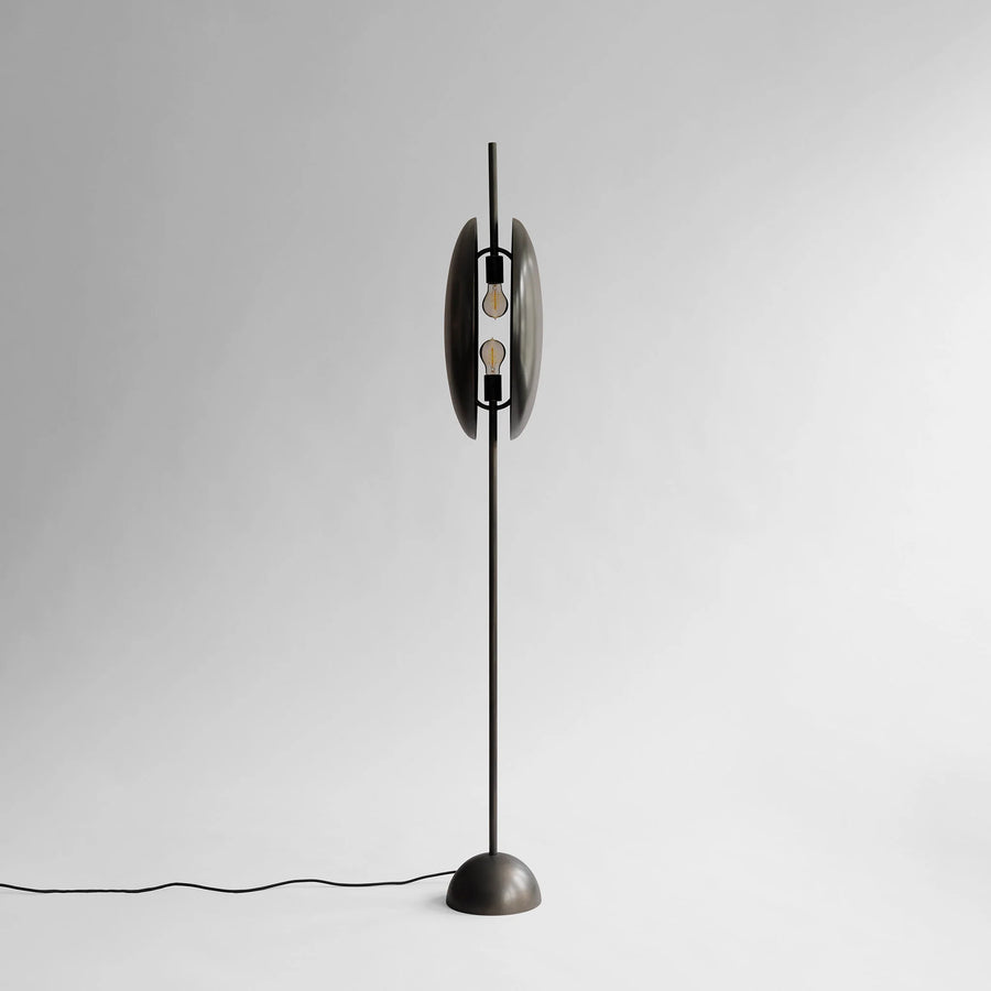 Side view of a modern floor lamp with a metallic base and cylindrical shade on a light gray background