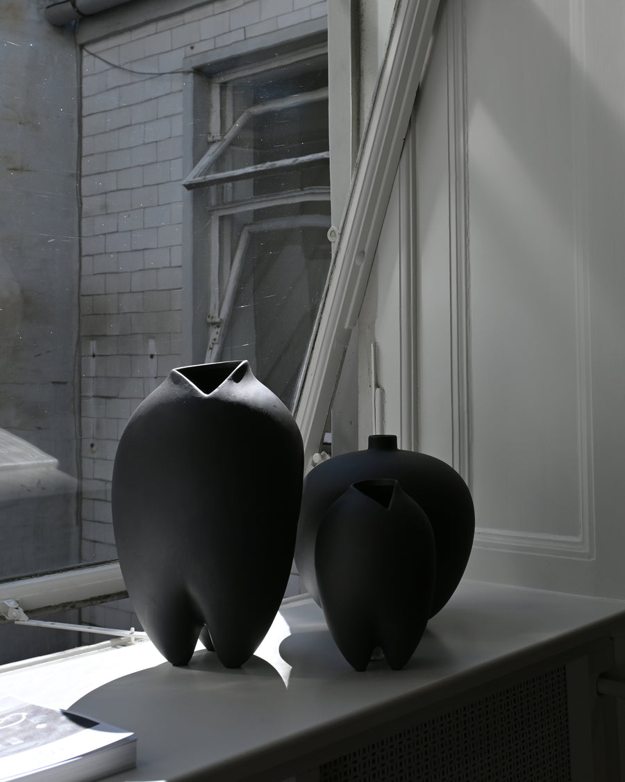 Two black ceramic vases on a windowsill with a building exterior in the background.