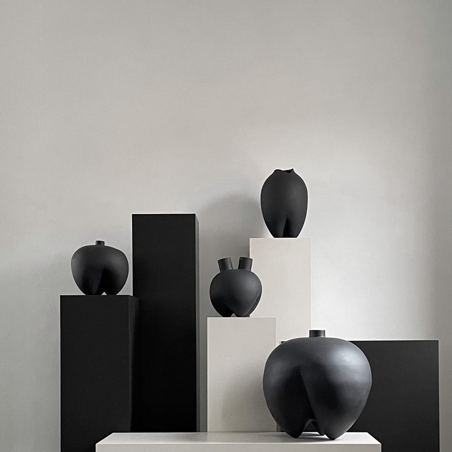 Black ceramic vases on white and black pedestals against a neutral background