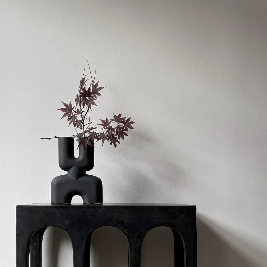 An organic-shaped 101Cph Cobra Double Mini Coffee 212002 vase sits on a table in an interior setting next to a white wall.