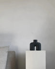A quirky black vase, the 101Cph Cobra Uno Mini Black 203024 by 101 Copenhagen, is elegantly displayed on a table beside a chic white couch.