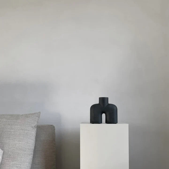 A quirky black vase, the 101Cph Cobra Uno Mini Black 203024 by 101 Copenhagen, is elegantly displayed on a table beside a chic white couch.