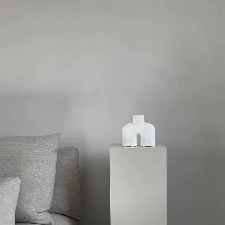 A grey couch with a 101Cph Cobra Uno Mini Bubble White 203021 vase next to it. The 101Cph Cobra Uno Mini Bubble White 203021 vase adds a touch of elegance to the space, perfectly complementing the sleek design of the Cobra Uno Mini Bubble couch by 101 Copenhagen.