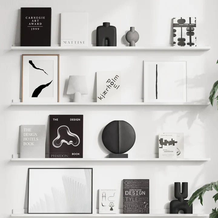 A white shelf with black and white art, a plant, and quirky 101Cph Guggenheim Mini Coffee 111220 vases.
