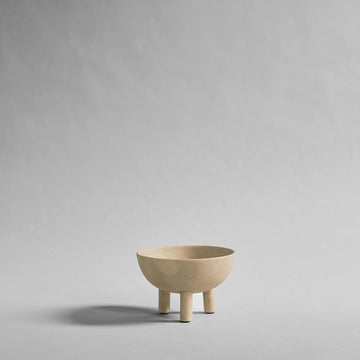 Beige ceramic bowl with three legs on a gray background from 101 Copenhagen at Spacio retail stores in Mumbai & Kolkata. 