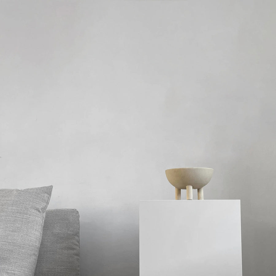 Small ceramic bowl on a white pedestal against a plain wall with a gray cushioned chair from 101 Copenhagen at Spacio retail stores in Mumbai & Kolkata. 