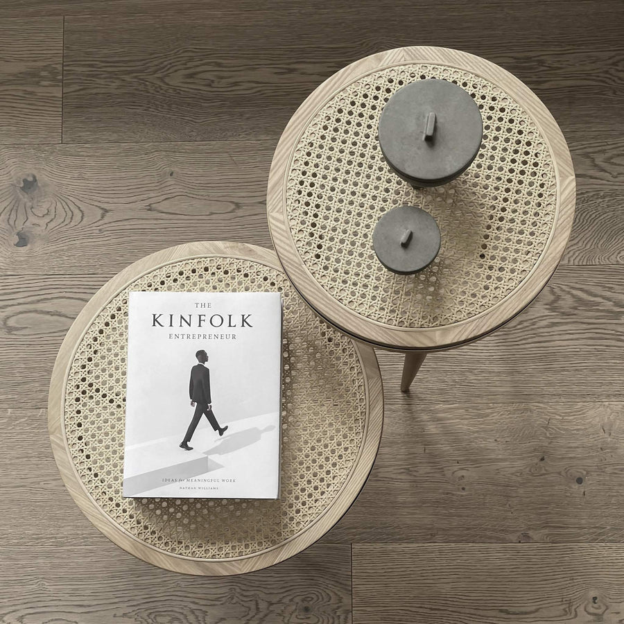 Round woven coffee table with a book titled 'The Kinfolk Entrepreneur' on a wooden floor from 101 Copenhagen at Spacio retail stores in Mumbai & Kolkata. 