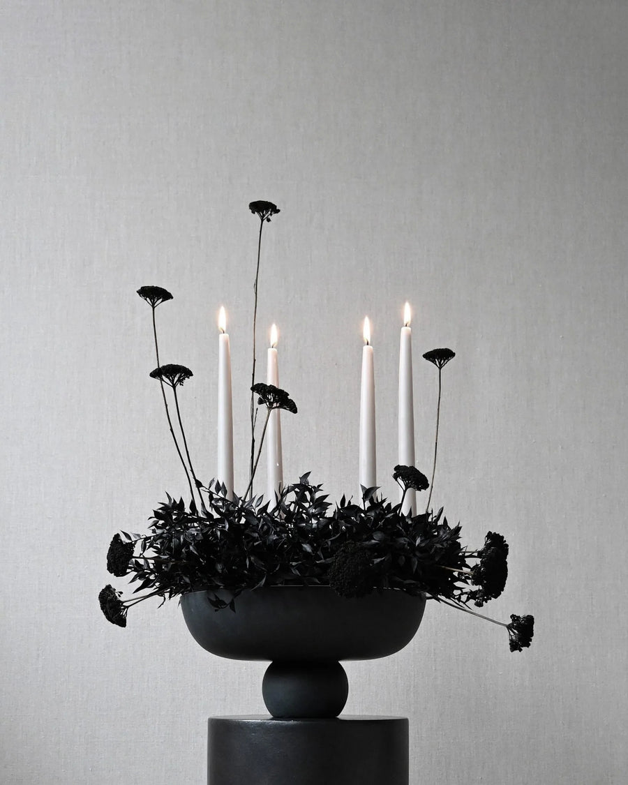 Candle holder with black flowers on a gray background in a ceramic bowl from 101 Copenhagen at Spacio retail stores in Mumbai & Kolkata. 