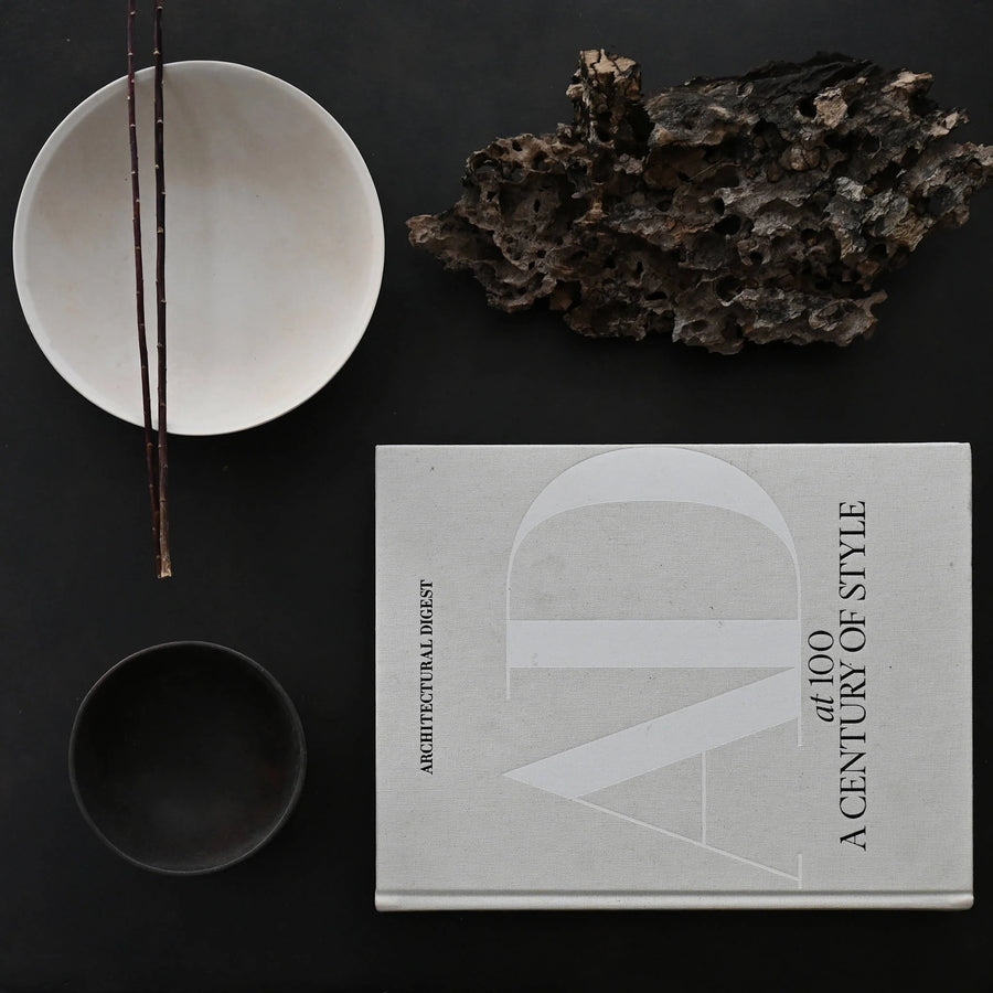 Book titled 'A Century of Style' by Architectural Digest on a dark surface with decorative items from 101 Copenhagen at Spacio retail stores in Mumbai & Kolkata. 