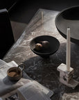 Table setting with a newspaper, cup of coffee, bowl, and candle on a dark marble surface from 101 Copenhagen at Spacio retail stores in Mumbai & Kolkata. 
