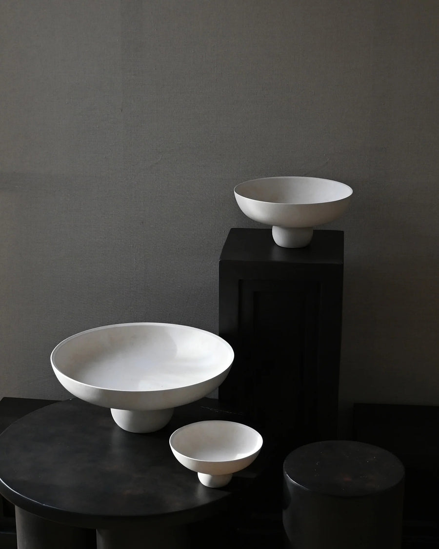 Three white ceramic bowls of varying sizes on a dark surface with a dark gray background from 101 Copenhagen at Spacio retail stores in Mumbai & Kolkata. 