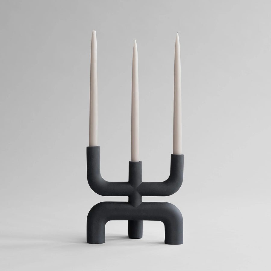 Black modern candle holder with three candles on a gray background from 101 Copenhagen at Spacio retail stores in Mumbai & Kolkata. 