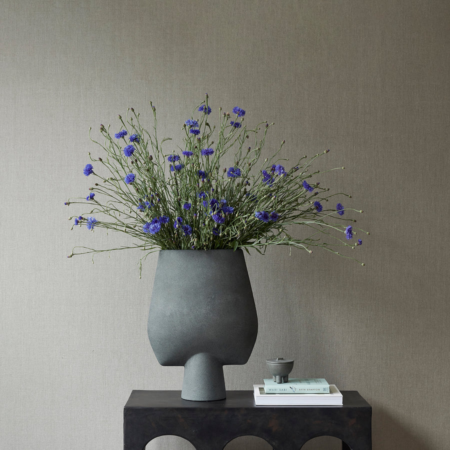 Gray vase with purple flowers on a dark surface against a gray wall from 101 Copenhagen at Spacio retail stores in Mumbai & Kolkata. 