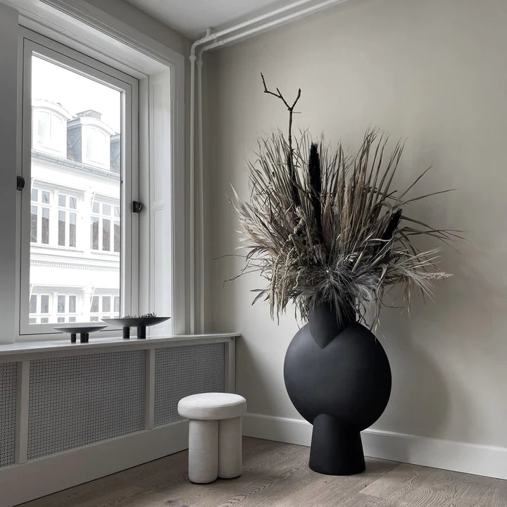 A black 101 Copenhagen vase sits next to a window in a room.