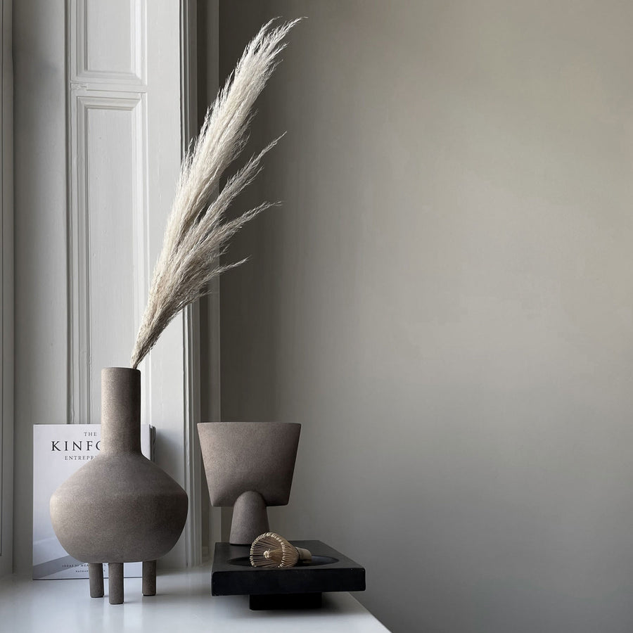 A quirky vase, the 101Cph Duck Vase Fat Taupe 213045, sits on a window sill next to a book.