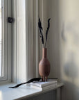 A 101Cph Duck Vase Slim Terracotta 213044, made by 101 Copenhagen, sits on a window sill next to a book.