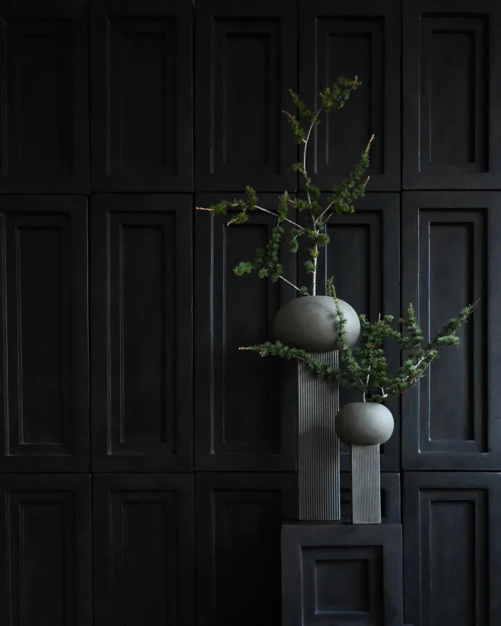 Two ceramic 101Cph Empire Big Dark Grey 223034 vases with a plant on them in front of a black wall, featuring architectural references.