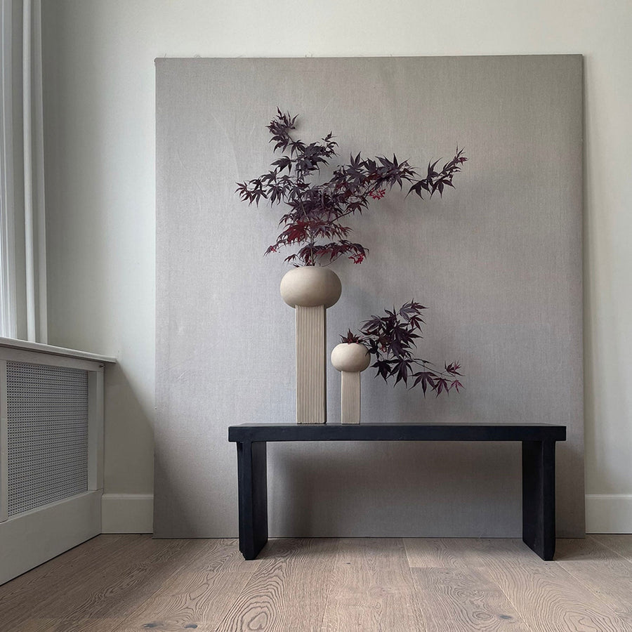 A table with two quirky vases, 101 Copenhagen Empire Mini Sand 223037, and a painting on the wall.