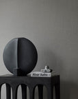 A quirky 101Cph Guggenheim Big Black 203004 vase by 101 Copenhagen sits on a table next to a book in an interior setting.