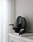 A quirky 101Cph Guggenheim Big Black 203004 vase by 101 Copenhagen sits on a mantle in an interior setting.