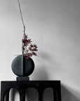 The 101Cph Guggenheim Mini Black 111126 vase by 101 Copenhagen sits on a wooden table in an interior setting.